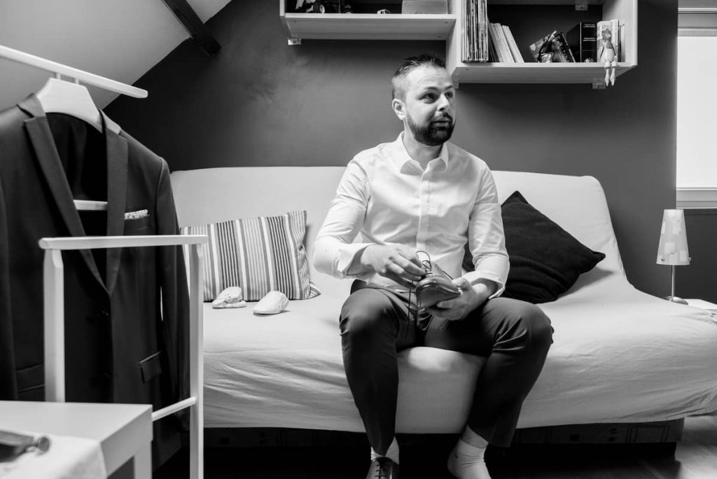 Préparatifs de mariage : le marié assis sur un canapé enfile ses chaussures