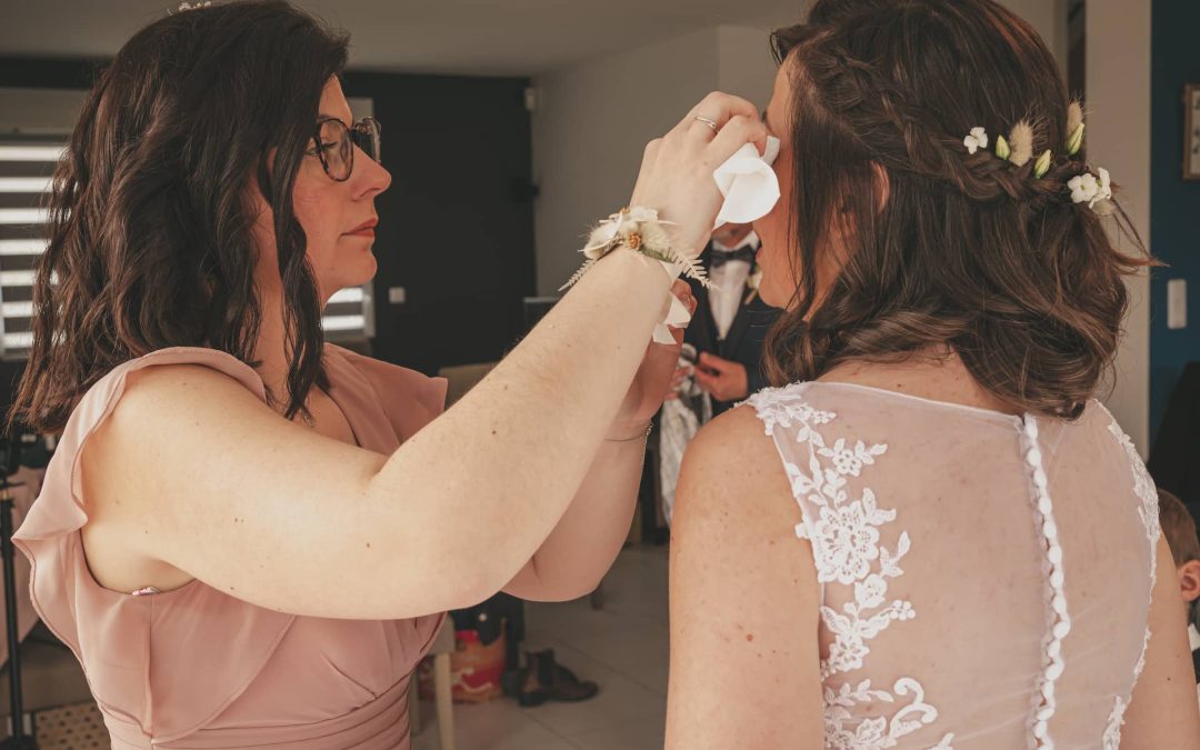 Une femme en robe de mariée avec des fleurs dans les cheveux, une autre personne lui essuie les larmes.