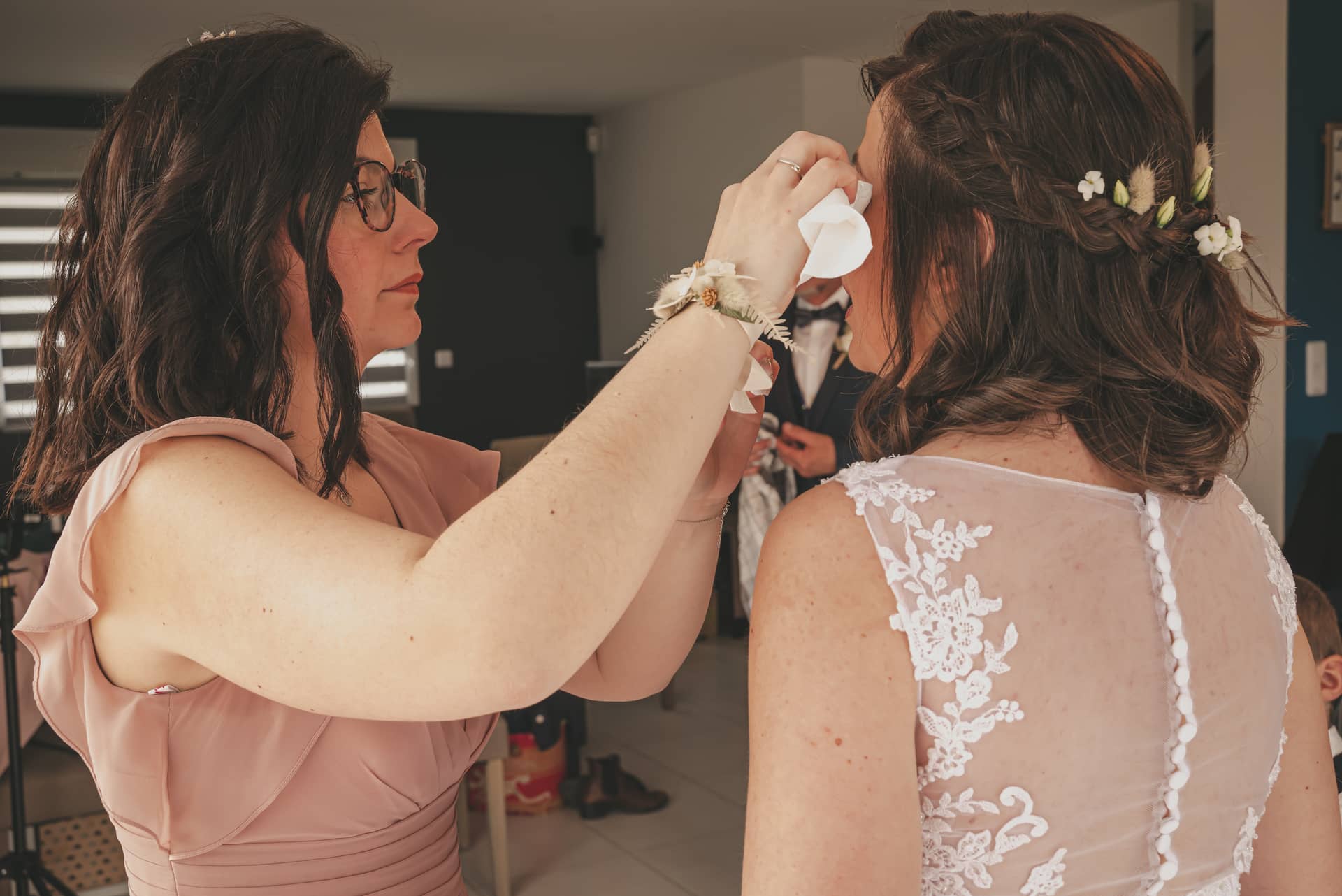 Une femme en robe de mariée avec des fleurs dans les cheveux, une autre personne lui essuie les larmes.
