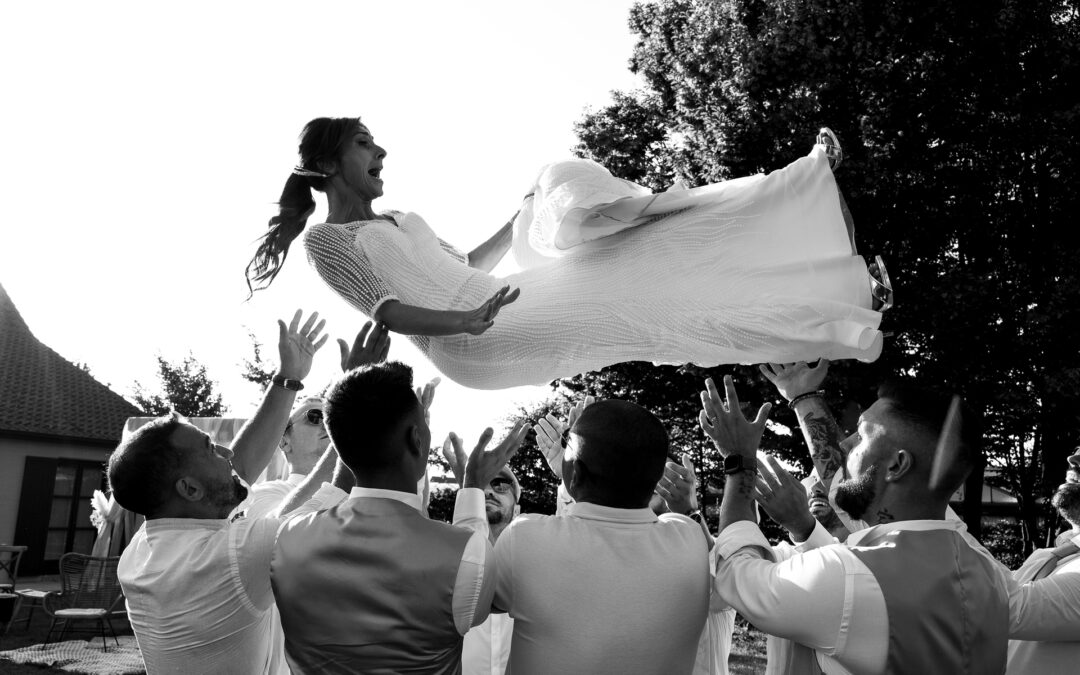 Une mariée est joyeusement soulevée dans les airs par des invités lors d’une cérémonie de mariage en plein air.