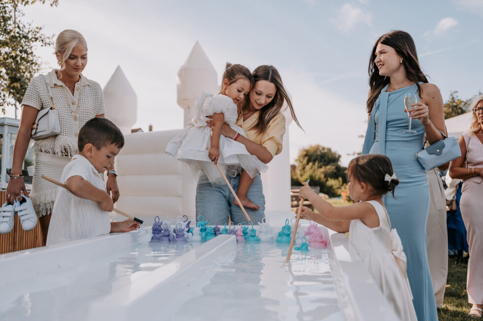Enfants jouant à la pêche aux canards lors du vin d'honneur, avec un château gonflable blanc en arrière-plan.