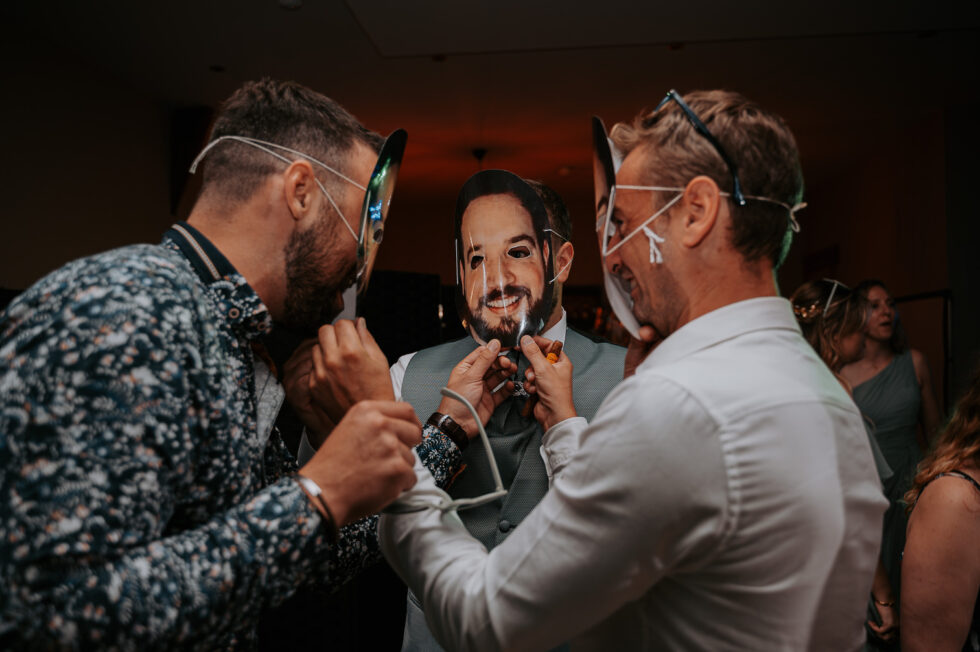 Trois hommes portent des masques en carton à l'effigie du visage du marié lors d'une animation surprise.