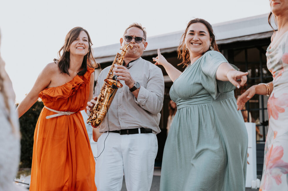 Un saxophoniste anime le vin d'honneur en jouant au milieu des invités qui dansent.