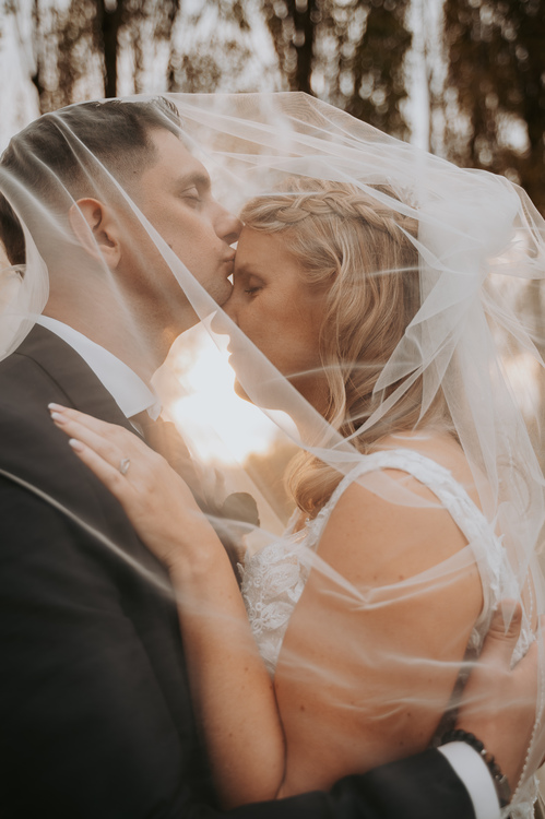 Marié embrassant tendrement la mariée sur le front sous le voile. Illustration d'un avis client élogieux pour Benoit Delattre, photographe mariage dans le Nord.
