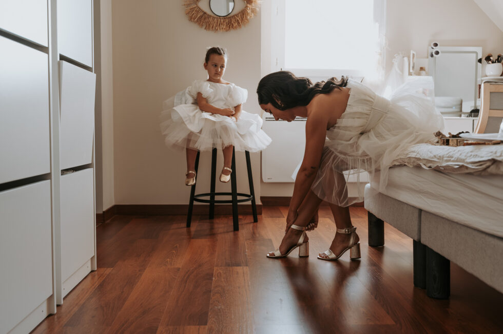 Petite fille d'honneur assise sagement sur un tabouret noir regardant la mariée se préparer.