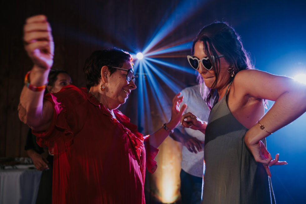 Une dame en robe rouge et une jeune femme dansent ensemble en riant, toutes deux portant des lunettes fun.