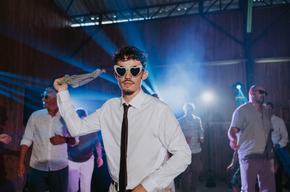 Un invité danse énergiquement avec des lunettes de soleil en forme de cœur blanc et fait tourner une étoffe en l'air.