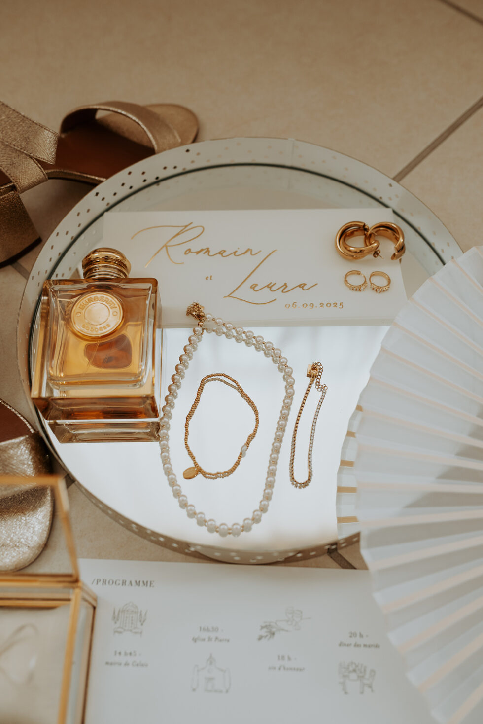 Mise en scène flatlay des bijoux de la mariée : colliers de perles et bracelets dorés sur un miroir.