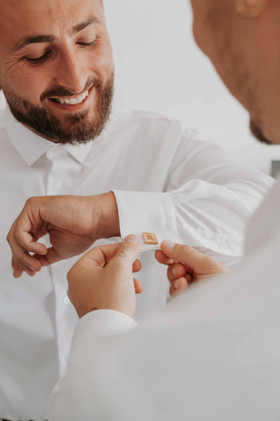 Gros plan sur les mains du marié attachant un bouton de manchette carré et doré personnalisé.