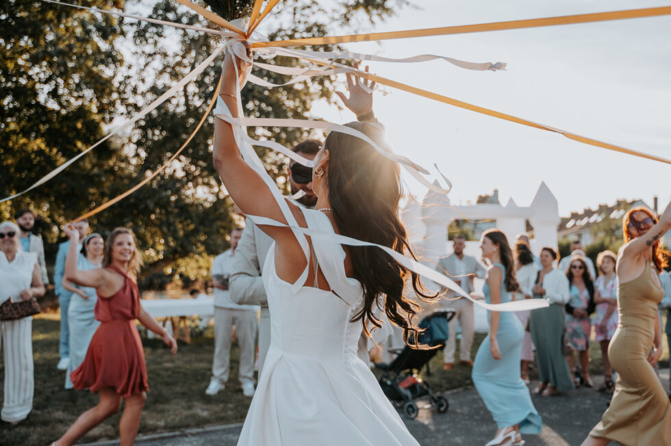 La mariée anime le jeu du ruban pour désigner celle qui gagnera le bouquet, sous un beau soleil.