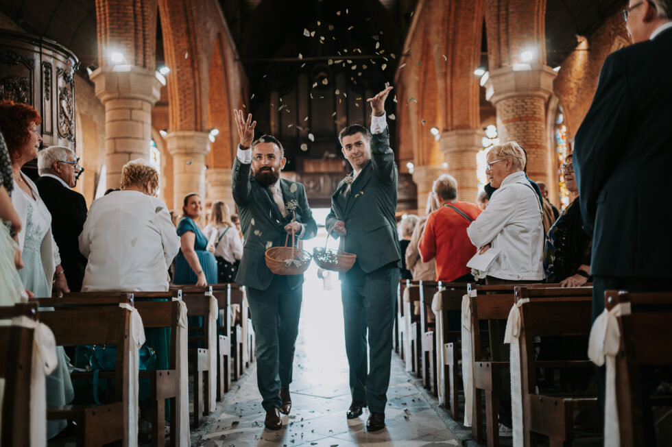 Deux témoins lancent joyeusement des pétales/feuilles en l'air dans l'allée centrale de l'église.