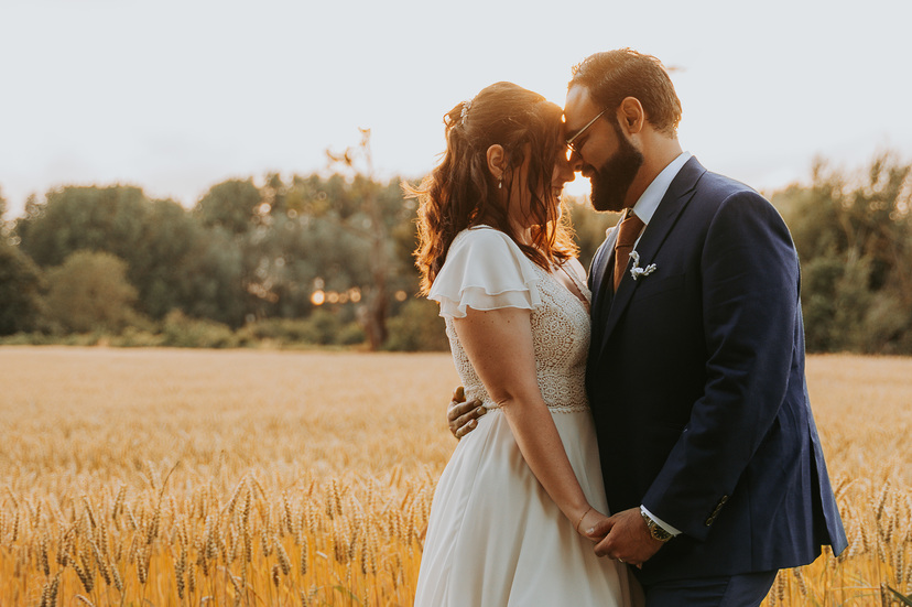 Couple de mariés s'enlaçant au milieu d'un champ de blé doré au crépuscule.