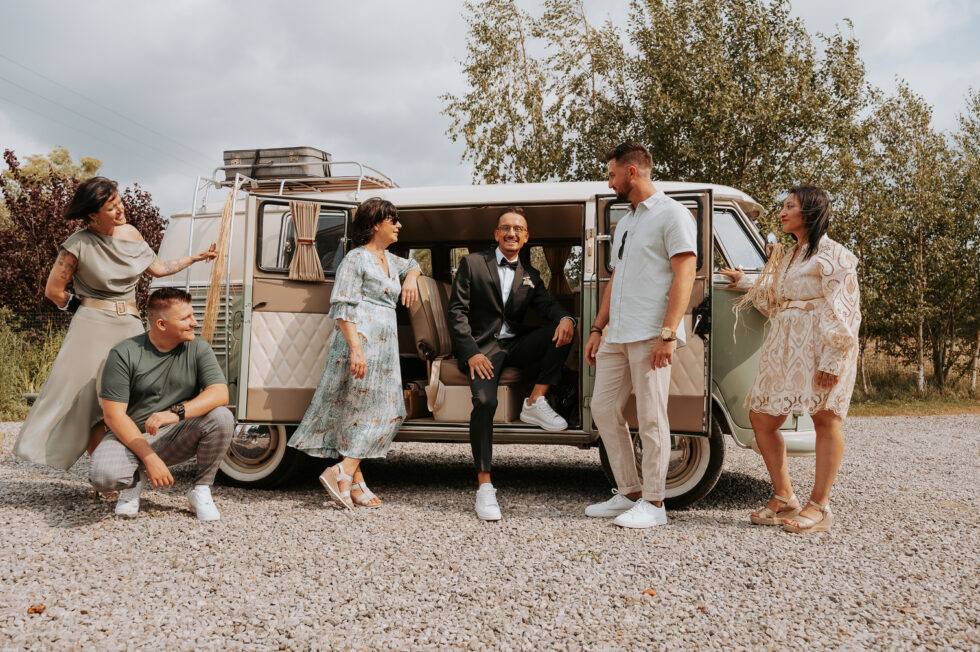 Le marié assis dans un Combi Volkswagen vintage beige et vert, entouré de ses amis qui posent de manière décontractée.