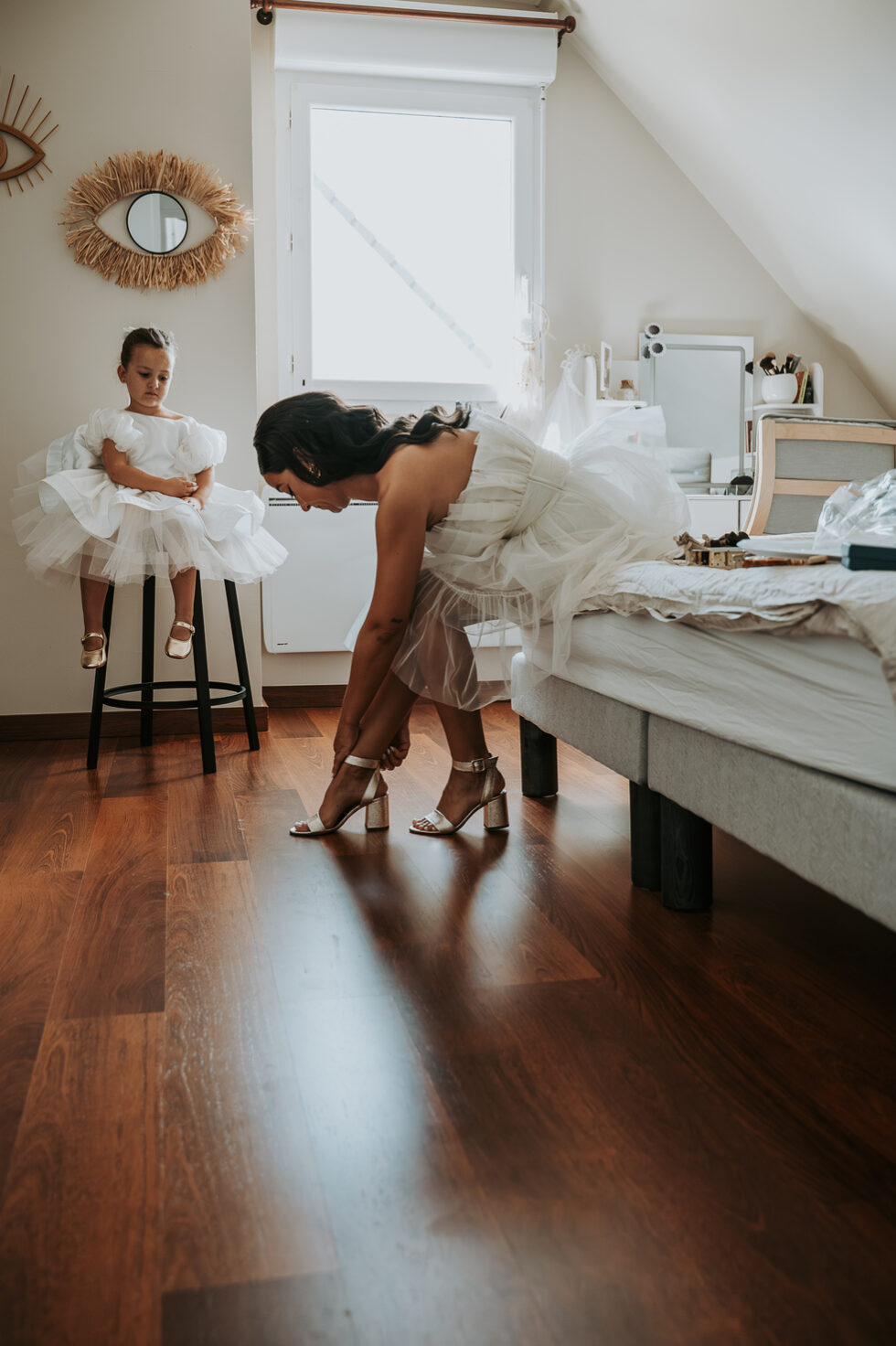 La mariée en robe courte et tulle enfile ses sandales dorées sous le regard d'une petite fille.