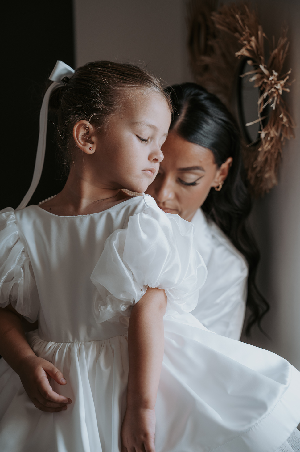 La mariée aide une petite fille d'honneur à fermer sa robe blanche, moment de tendresse.