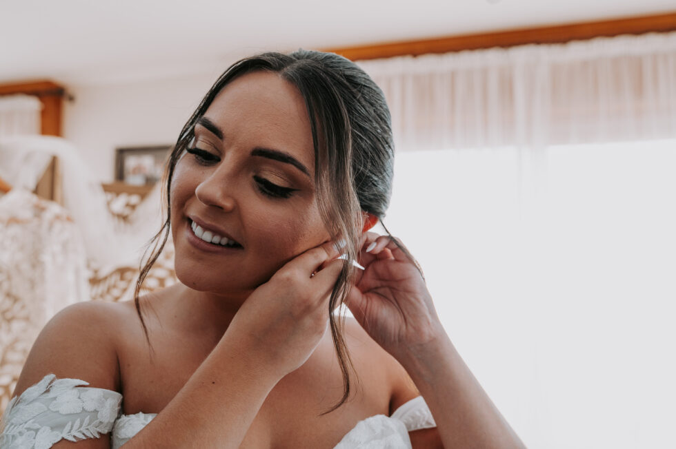 La mariée souriante ajuste ses boucles d'oreilles pendant ses préparatifs.
