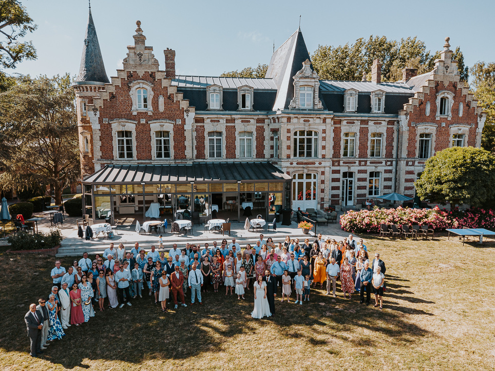 Vue aérienne par drone de tous les invités et mariés devant un château en briques rouges dans le Nord.