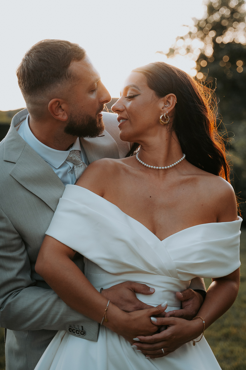 Portrait romantique du couple baigné par la lumière dorée du coucher de soleil, la mariée en robe col bateau.