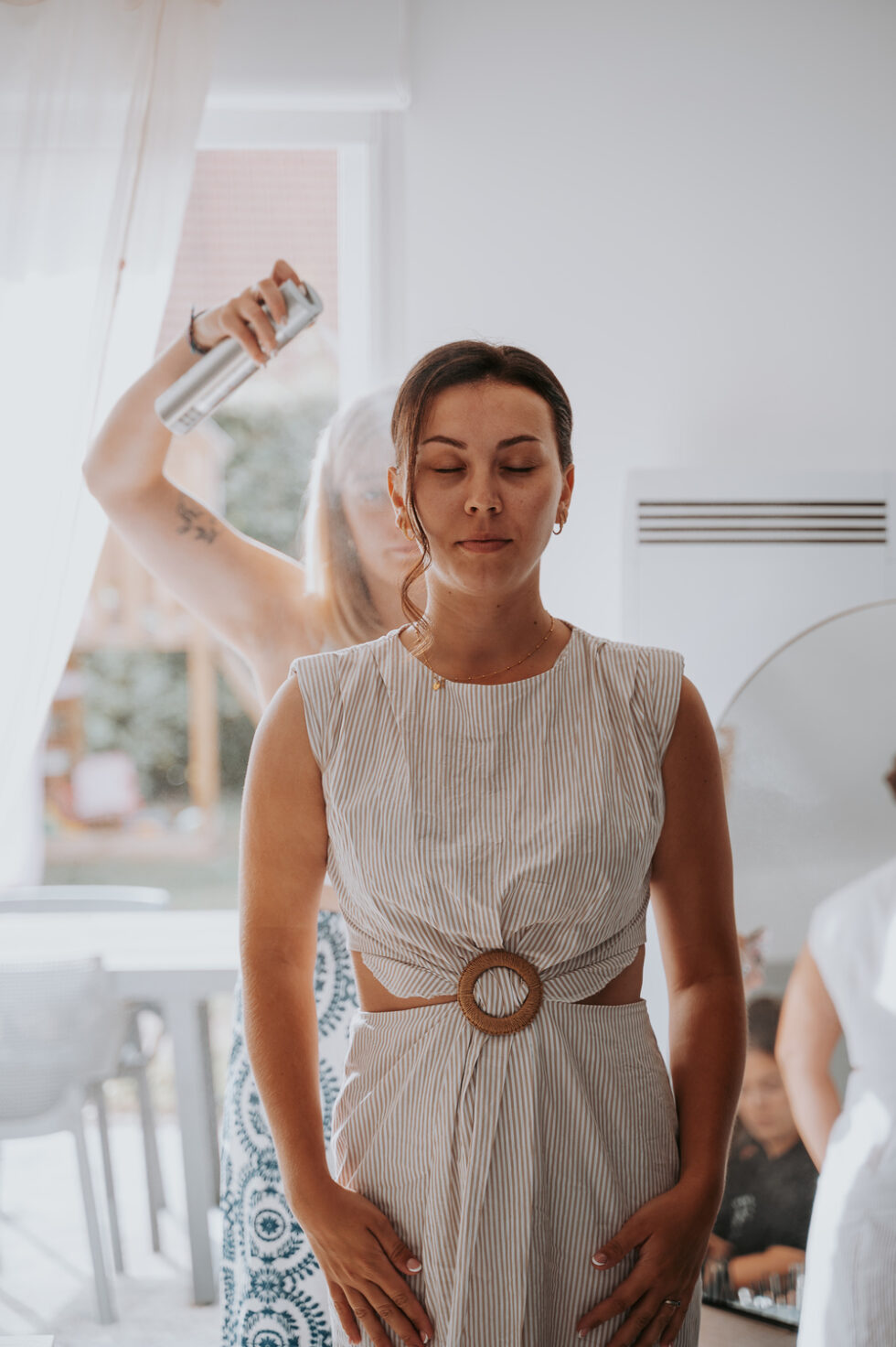 La coiffeuse vaporise de la laque pour fixer la coiffure de la mariée lors des préparatifs.
