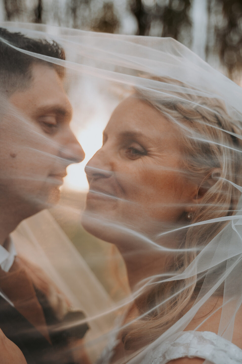 La mariée et le marié se regardant intensément les yeux dans les yeux sous le voile transparent.