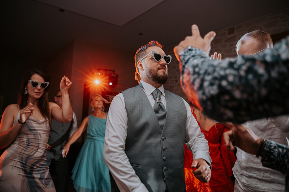 Le marié met l'ambiance sur la piste de danse en portant des lunettes de soleil en forme de cœurs blancs.