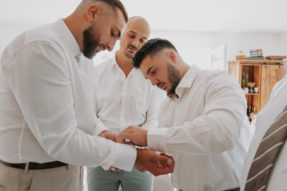 Les témoins en chemise blanche aident le marié à ajuster ses poignets de chemise.