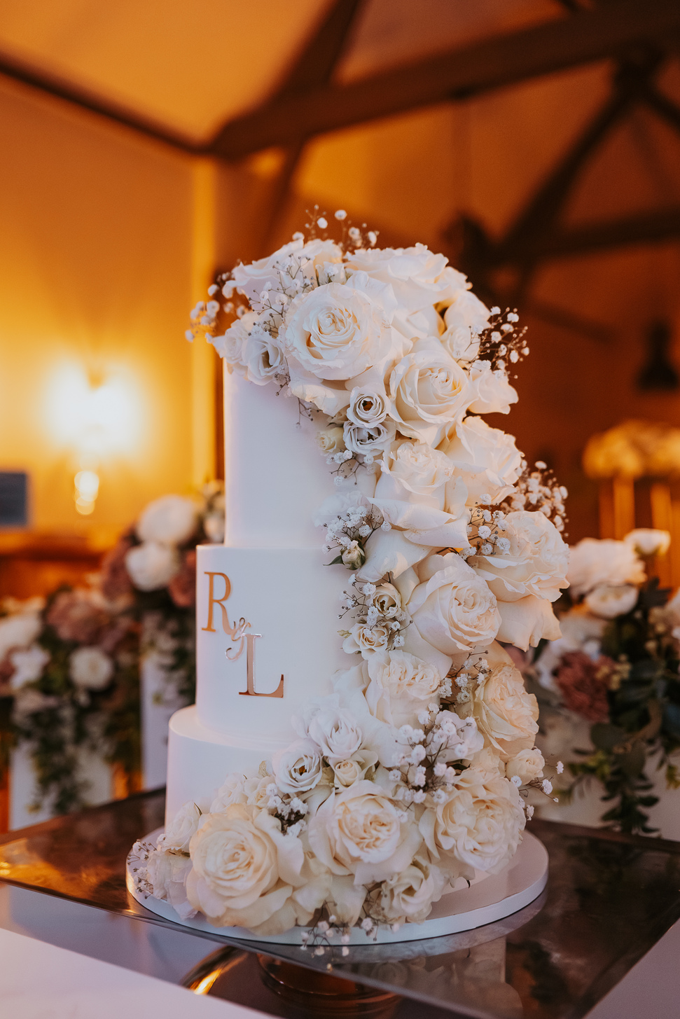 Wedding cake blanc à trois étages décoré d'une cascade de roses blanches et des initiales R & L dorées.